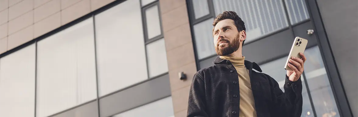 Eine Person steht vor einem Bürogabäude und hält ein Smartphone in der Hand.